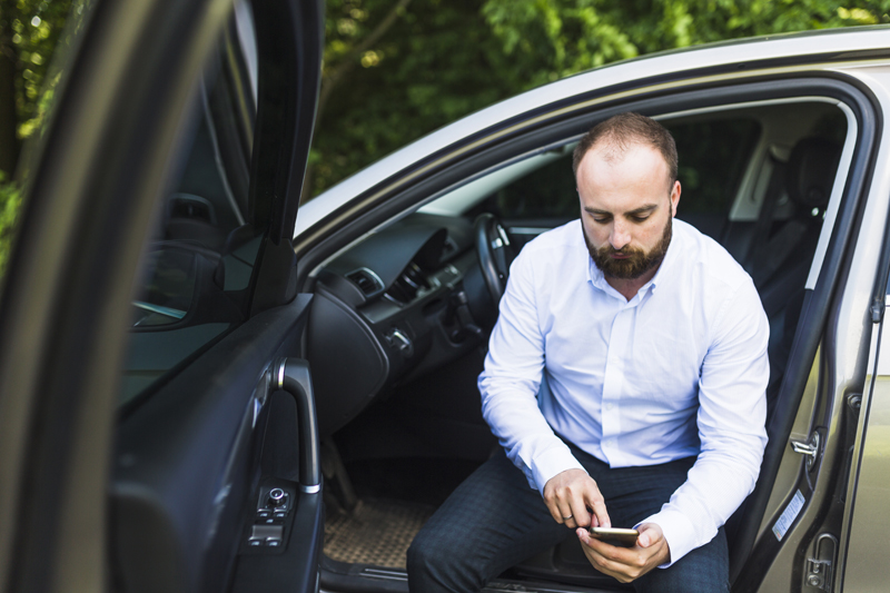 man-sitting-in-a-car-with-open-door-looking-at-mobile-phone-screen.jpg