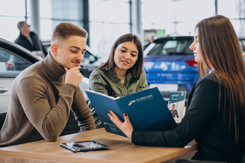 young-couple-talking-to-a-sales-person-in-a-car-showroom.jpg